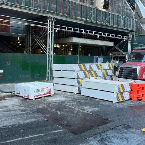 Flatbed with Durock and sheetrock pallets next to a boom truck at a job site